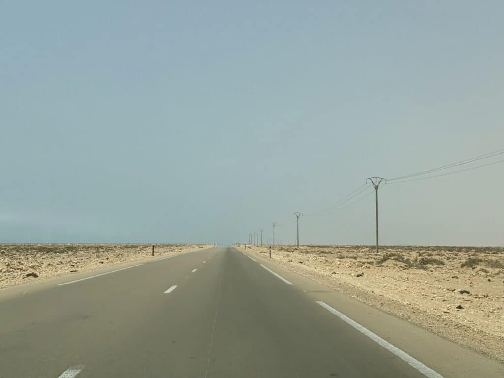 Recta infinita en medio del desierto con efecto de espejismo sobre el asfalto, bajo un cielo azul pálido