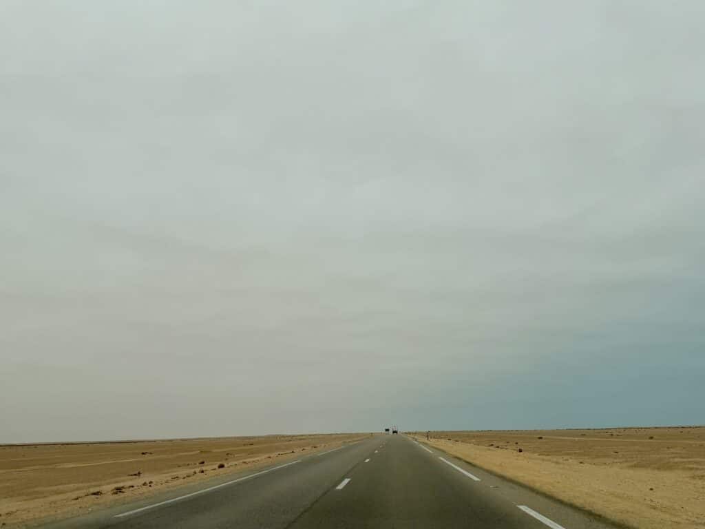 Carretera recta que se pierde en el horizonte en medio del desierto, bajo un cielo nublado, en el tramo entre El Aaiún y Dakhla