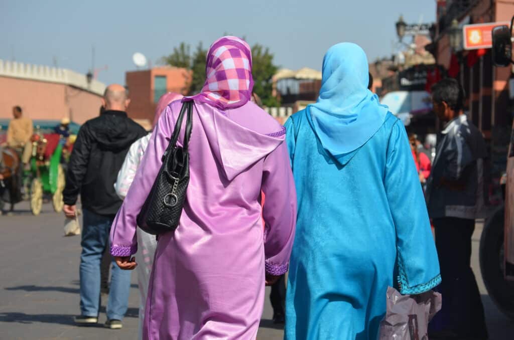 Dos mujeres vestidas con djellabas coloridas y pañuelo caminando por una calle en Marruecos