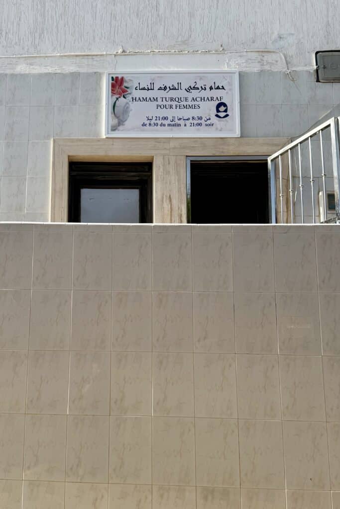 Cartel en árabe y francés del hammam tradicional marroquí para mujeres, en una fachada sencilla con azulejos