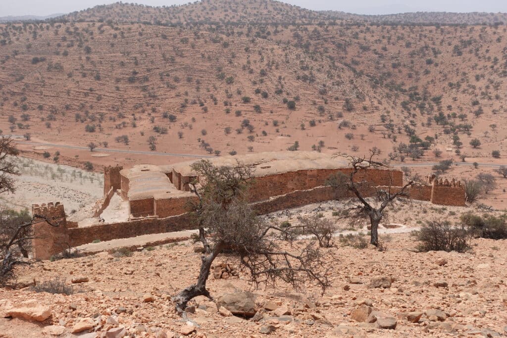 Granero fortificado visto desde la distancia, rodeado de árboles de argán y paisaje montañoso del Anti-Atlas
