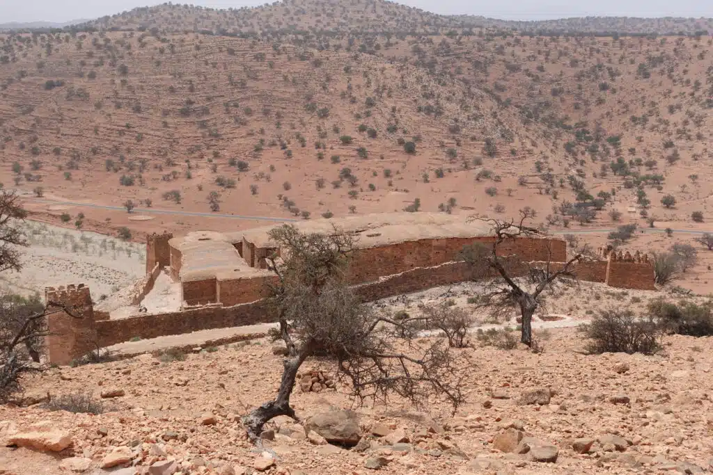 Granero fortificado visto desde la distancia, rodeado de árboles de argán y paisaje montañoso del Anti-Atlas