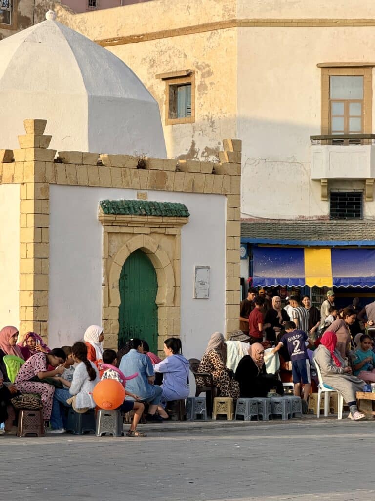 Grupo de mujeres y niñas marroquíes sentadas en la calle pintándose las manos con henna en Essaouira, en la víspera del Eid al-Adha.