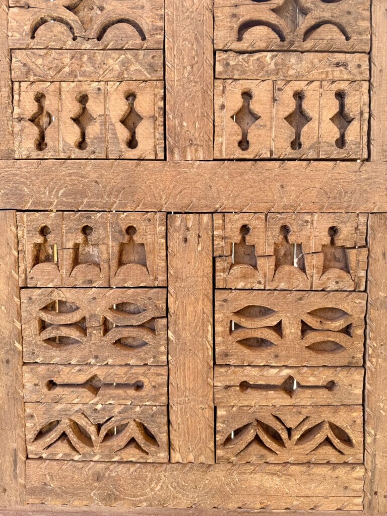 Detalle de puerta de madera tallada con motivos geométricos tradicionales, posiblemente parte de una ventana o armario