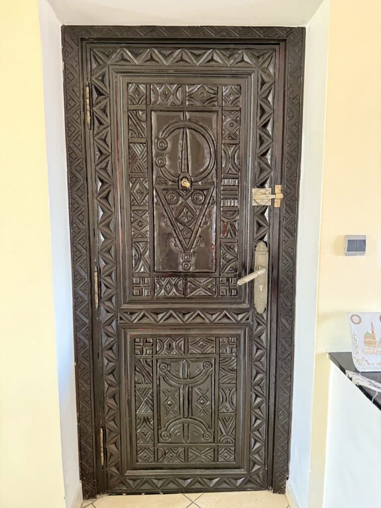 Puerta de madera tallada con motivos geométricos amazigh y cerradura metálica, en el interior de una casa marroquí.