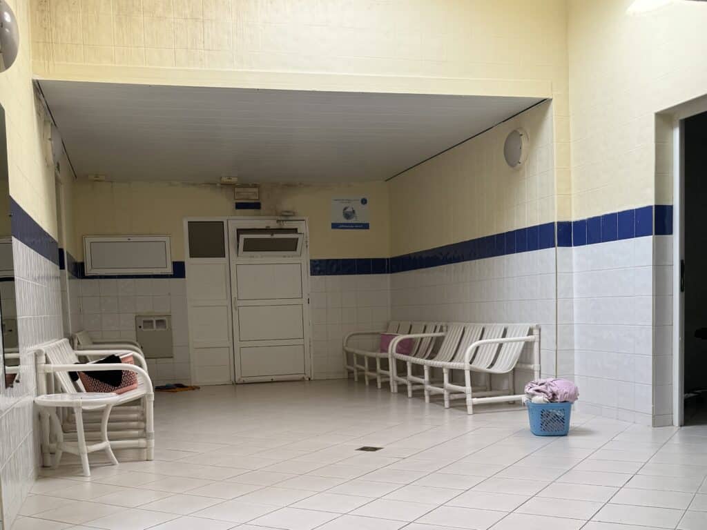 Interior del hammam tradicional marroquí para mujeres, con bancos de plástico blanco, cestos con toallas y ambiente sencillo y limpio