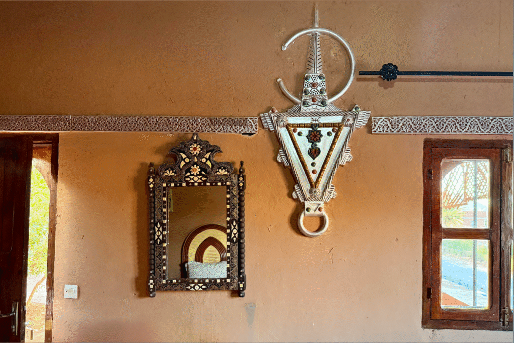 Interior de una casa tradicional marroquí con un espejo decorado y un gran colgante amazigh en la pared, junto a una ventana de madera.