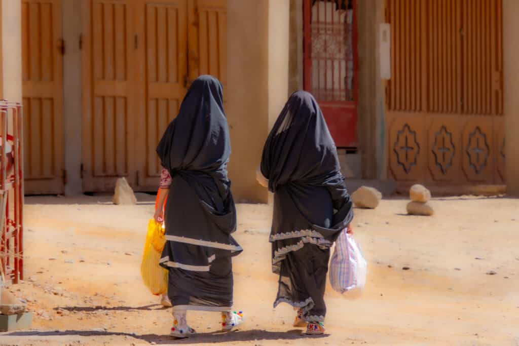 Dos mujeres amazigh vestidas con tamlḥaft negro caminando por una calle de Tafraoute, sur de Marruecos